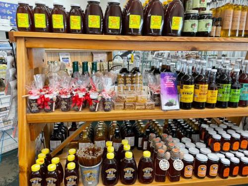 A wooden shelf displaying various jars of honey, syrups, and packaged treats in a store.