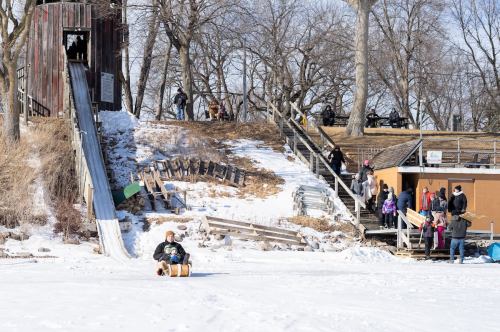 A snowy scene with children sledding down a hill, a playground slide, and people enjoying winter activities nearby.