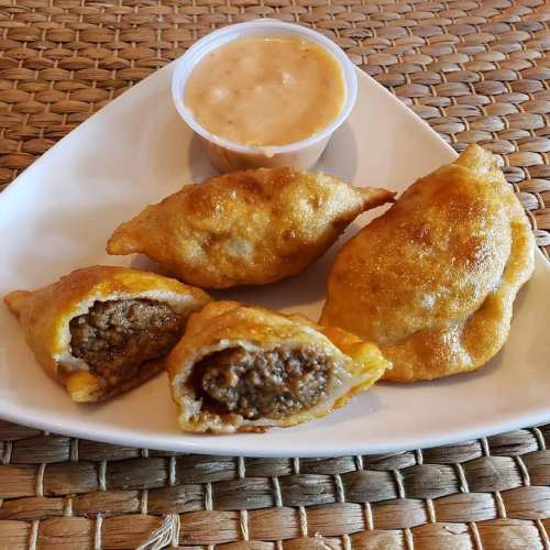 A plate of golden-brown fried pastries filled with meat, served with a small cup of dipping sauce.