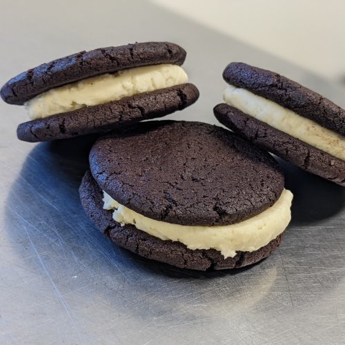 Three chocolate sandwich cookies with creamy filling, stacked on a metallic surface.
