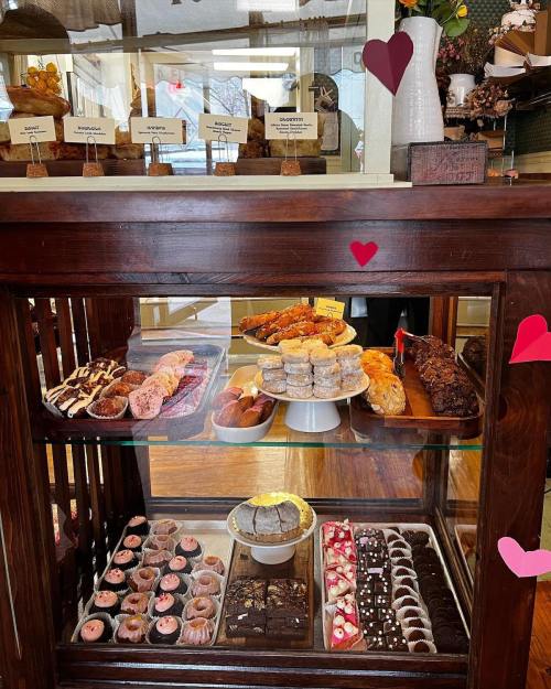A display case filled with various baked goods, including cookies, pastries, and cakes, decorated with heart shapes.