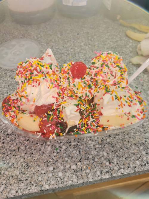 A colorful ice cream sundae topped with whipped cream, cherries, and a generous sprinkle of rainbow sprinkles.