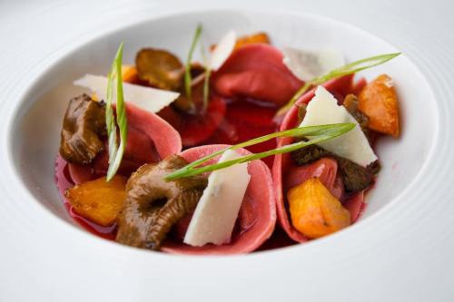 A gourmet dish featuring pink pasta filled with mushrooms and garnished with herbs and cheese, served in a vibrant sauce.