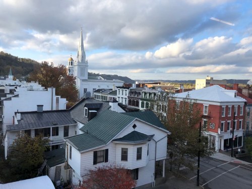 A scenic view of a small town with white buildings, a church steeple, and a cloudy sky in the background.