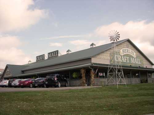 Exterior of Berlin Craft Mall featuring a large sign, a windmill, and parked cars on a grassy area.