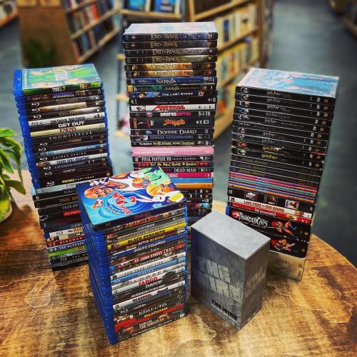 A collection of stacked DVDs and Blu-rays, featuring various movie titles, on a wooden table in a bookstore.