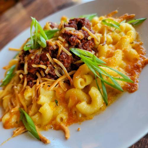 A plate of macaroni and cheese topped with chili, shredded cheese, and green onions.
