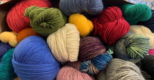 A colorful assortment of yarn balls in various textures and shades, piled together in a box.