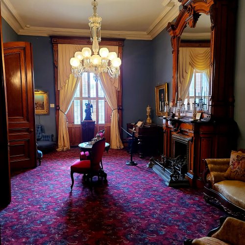 A vintage room with ornate furniture, a chandelier, and a fireplace, featuring rich red carpet and blue walls.