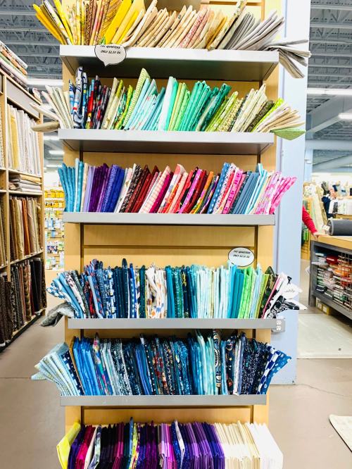 A colorful display of neatly folded fabric on shelves, showcasing a variety of patterns and textures.