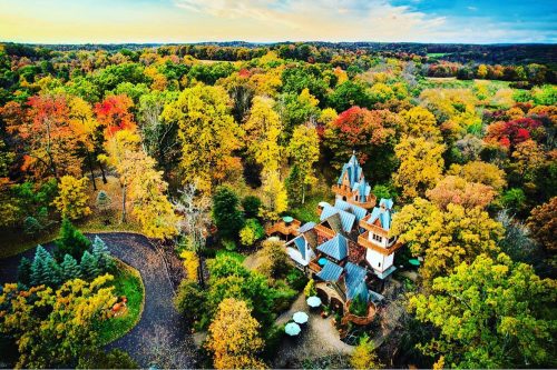 Aerial view of a colorful autumn forest with a whimsical house nestled among vibrant trees.