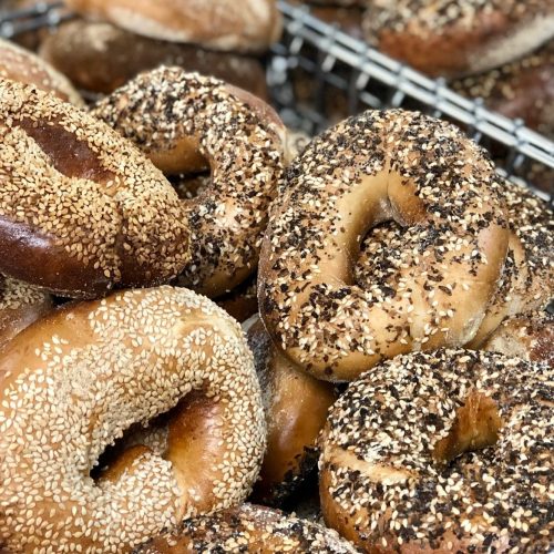 A close-up of assorted bagels topped with sesame seeds and various spices, piled in a basket.
