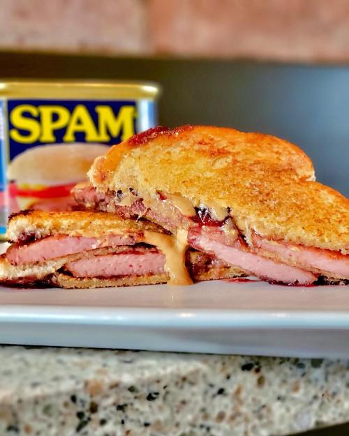 A close-up of a sandwich made with layers of Spam and peanut butter, served on a plate with a can of Spam in the background.