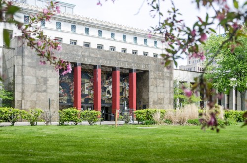 The entrance of the Detroit Public Library, framed by greenery and flowers, showcasing its architectural details.