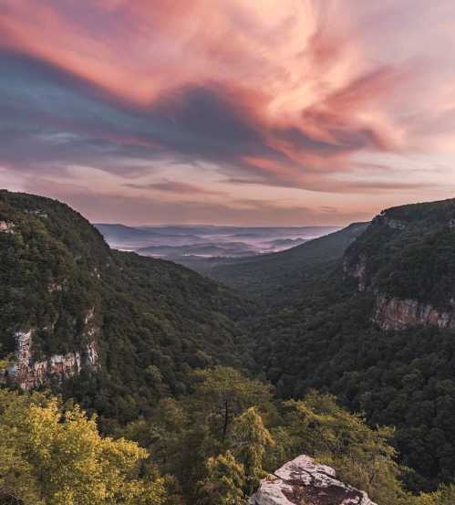 A scenic view of a lush green valley surrounded by mountains under a colorful sunset sky.