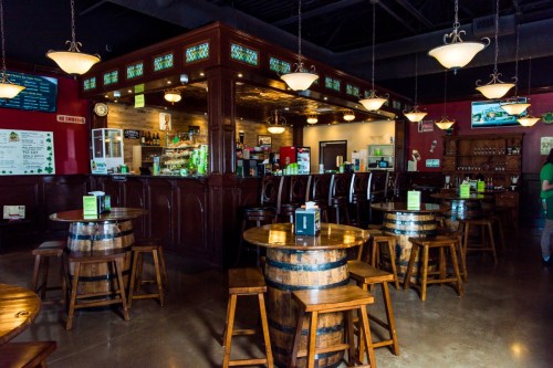 A cozy bar with wooden barrels as tables, pendant lights, and a well-stocked counter in a warm, inviting atmosphere.