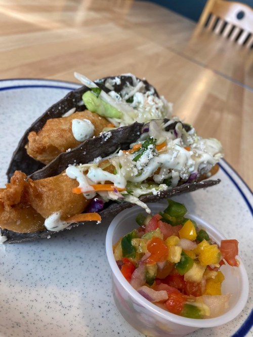 Three crispy tacos filled with fish and topped with slaw, served with a side of fresh salsa.