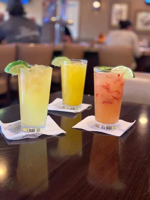 Three colorful cocktails with lime garnishes on a table, set in a restaurant atmosphere.