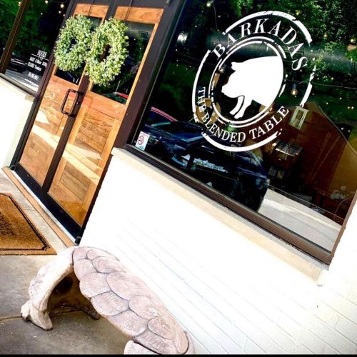 A wooden bench in front of a restaurant window featuring a logo that reads "Barkadas: The Blended Table."
