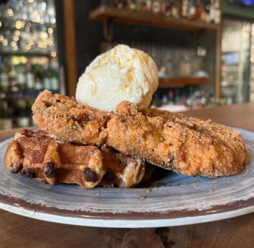 A plate featuring crispy fried chicken on waffles, topped with a scoop of vanilla ice cream.
