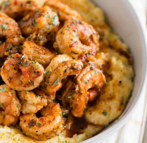 A bowl of creamy grits topped with seasoned shrimp and garnished with herbs.