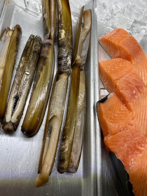 A tray with fresh seafood, including large clams and slices of salmon, resting on ice.