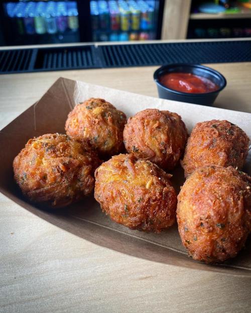 A tray of golden-brown, crispy fried balls with herbs, served with a small cup of red dipping sauce.