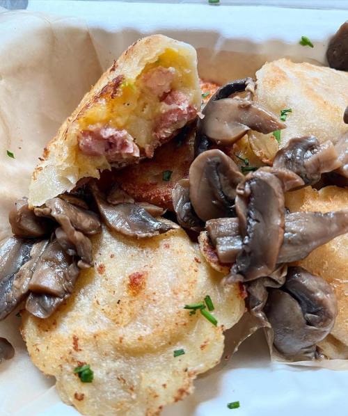 A close-up of crispy potato pancakes topped with sautéed mushrooms and a bite taken out, revealing a savory filling.