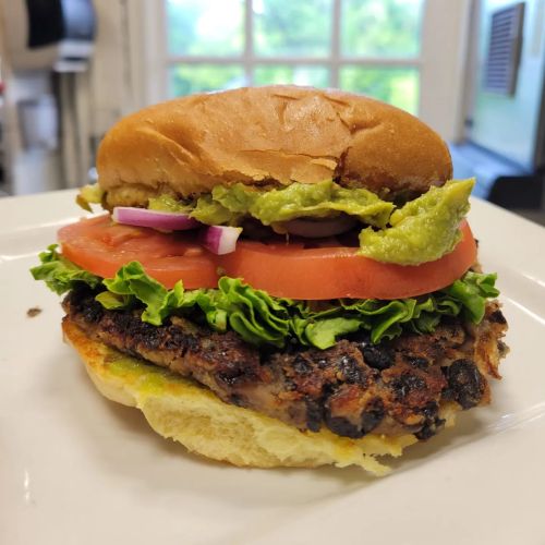 A close-up of a burger with a black bean patty, lettuce, tomato, onion, and guacamole on a toasted bun.