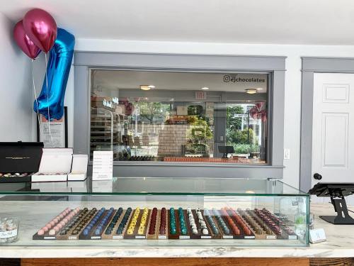 A display of colorful macarons in a chocolate shop, with balloons and a view of the shop's interior in the background.