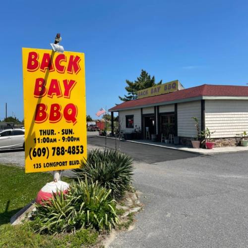 A restaurant exterior with a large sign reading "Back Bay BBQ," featuring hours and location details.