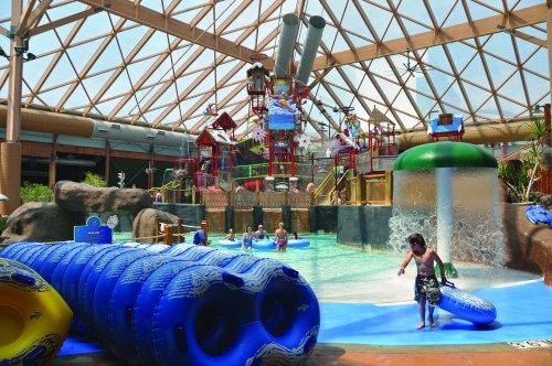 A vibrant indoor water park with slides, pools, and children playing in a tropical-themed environment.