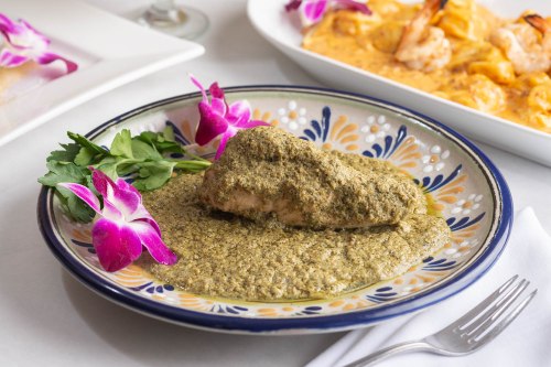 A plate of salmon in green sauce, garnished with herbs and purple orchids, served alongside a shrimp dish.