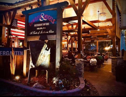 Sign for Cowboy & Angels restaurant in Helen, GA, with outdoor seating and a lively atmosphere in the evening.