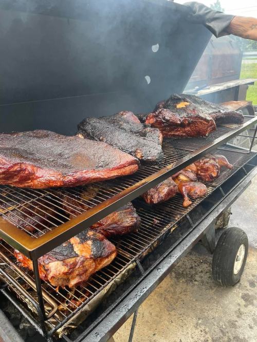 A barbecue grill filled with various meats, including brisket and chicken, smoking in a backyard setting.