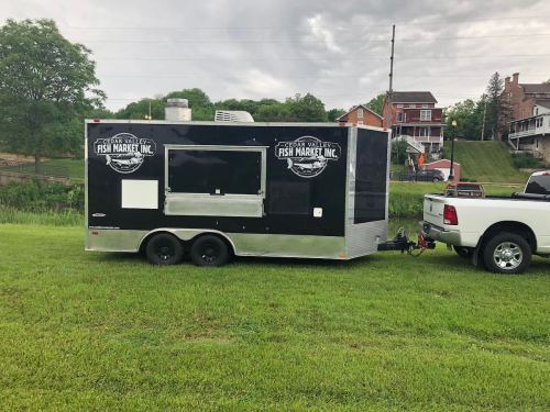 A black food trailer with "Fish Market Inc." signage parked on green grass near a residential area.