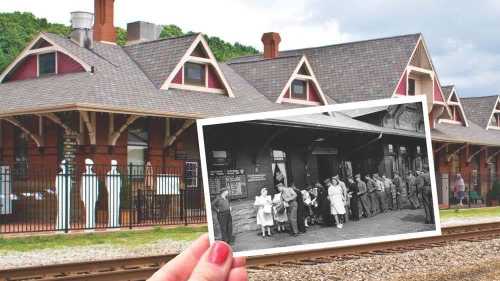 A hand holds a vintage photo of people at a train station in front of a modern station building.