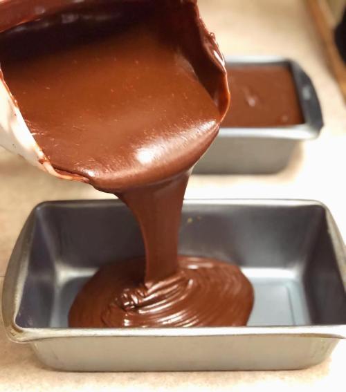 A bowl of chocolate batter is being poured into two metal loaf pans on a countertop.