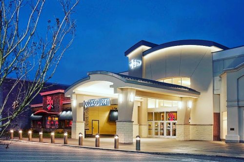 A brightly lit food court entrance at dusk, with nearby restaurants visible in the background.