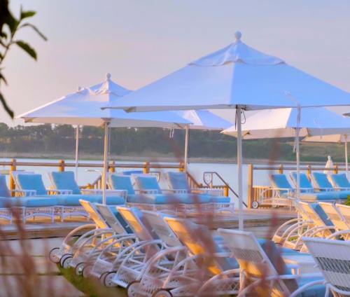 A serene lakeside scene with white lounge chairs and umbrellas under a pastel sky.