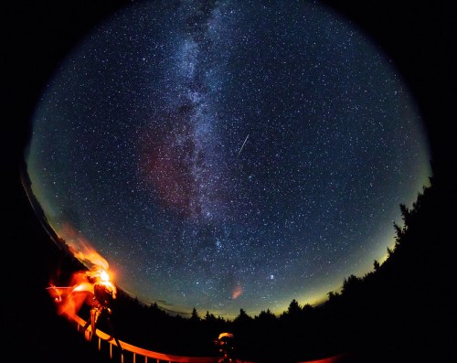 A starry night sky with the Milky Way and a shooting star, viewed from a dark outdoor location.
