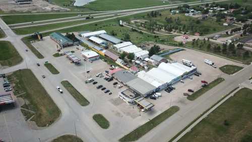 Aerial view of a small commercial area with various buildings, parking lots, and green fields in the background.