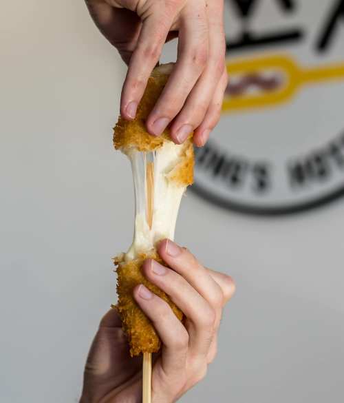 Two hands pull apart a crispy, golden-brown cheese stick, revealing gooey melted cheese in the center.
