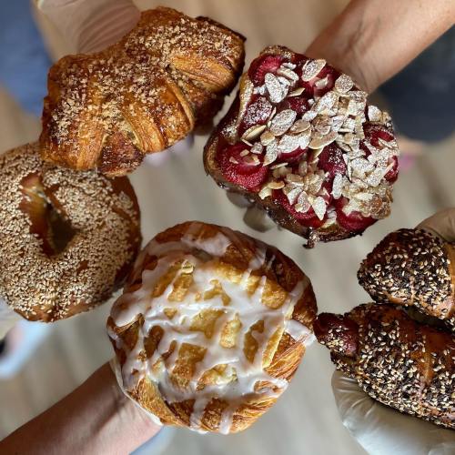 A group of hands holding various pastries, including croissants and a fruit-topped pastry, all beautifully presented.