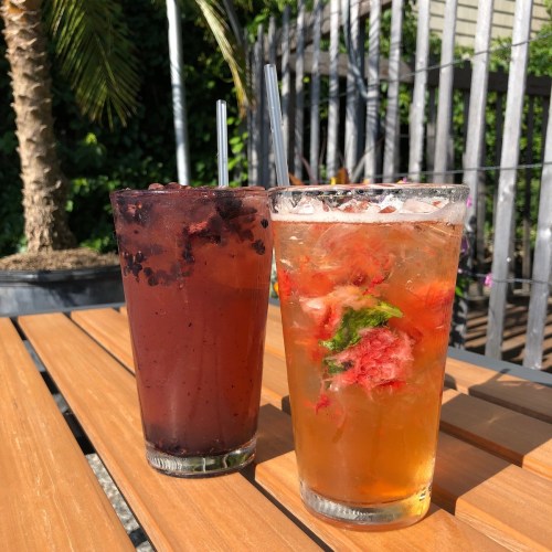 Two colorful drinks on a wooden table, one dark red with berries and the other light orange with mint and fruit.
