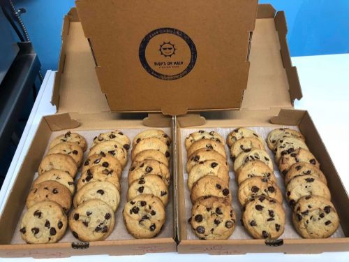 Two pizza boxes filled with freshly baked chocolate chip cookies, arranged neatly in rows.