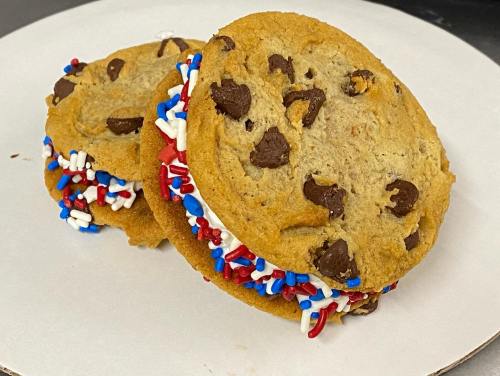Two chocolate chip cookie sandwiches filled with white cream and decorated with red, white, and blue sprinkles.