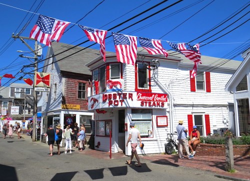 A charming street scene with a seafood restaurant, American flags, and people enjoying a sunny day.
