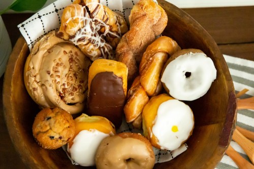 A wooden bowl filled with various donuts, pastries, and a cookie, arranged on a checkered napkin.