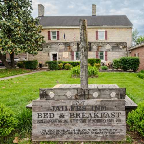 Historic building with a wooden sign reading "Jailer's Inn Bed & Breakfast," surrounded by greenery and trees.